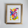 "Warhol Two, 2018" is an abstract alcohol ink painting featuring bold, vibrant colors of red, yellow, and blue. Swirls and splashes create a sense of movement. Mounted on a white background, and sitting in a gold frame.