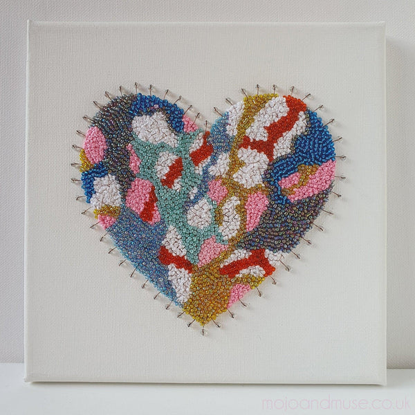 Abstract heart artwork with hand-embroidered beads and metallic threads on canvas, showcasing colorful and intricate design.