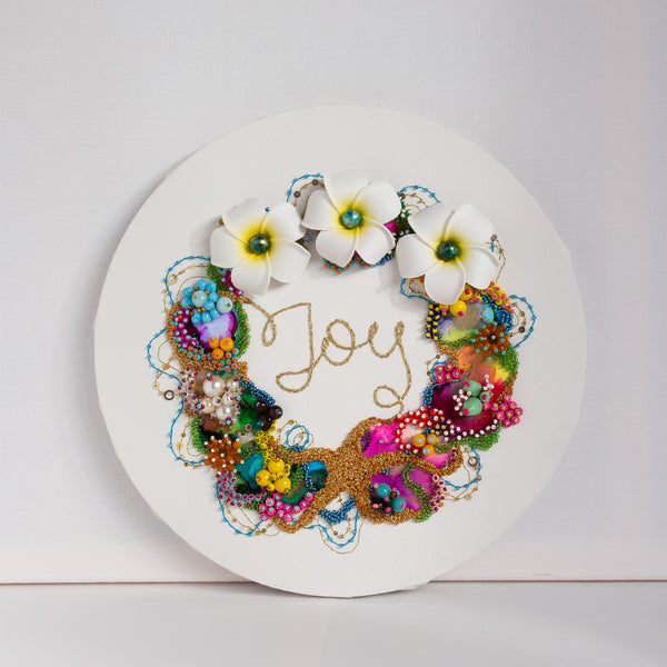 Abstract coral wreath artwork featuring intricate beadwork, embroidery, and alcohol ink on a 12” canvas. The design incorporates gold metallic threads and faux flowers, creating a textured, vibrant piece inspired by tropical reefs.