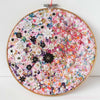 Close-up of "Flora 1.0" artwork, featuring hand-embroidered lace flowers, beads, and metallic threads on felt, with a gold-painted wooden hoop.