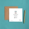 Square card back with colorful logo, product details, and contact info beside a brown kraft envelope and gold pen on teal fabric