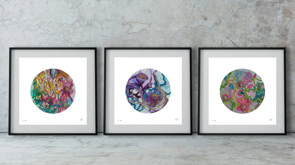 Three framed abstract circular artworks with colorful swirling patterns displayed on a concrete floor against a textured wall.