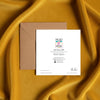 Square card back with colorful logo, artist details, and contact information beside a brown kraft envelope on gold satin fabric
