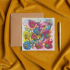 Square greeting card with intricate colorful floral embroidery paired with a kraft paper envelope and gold pen on mustard fabric