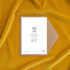 Square card back with colorful logo, artist credit, and contact details on white cardstock beside a kraft envelope on mustard fabric