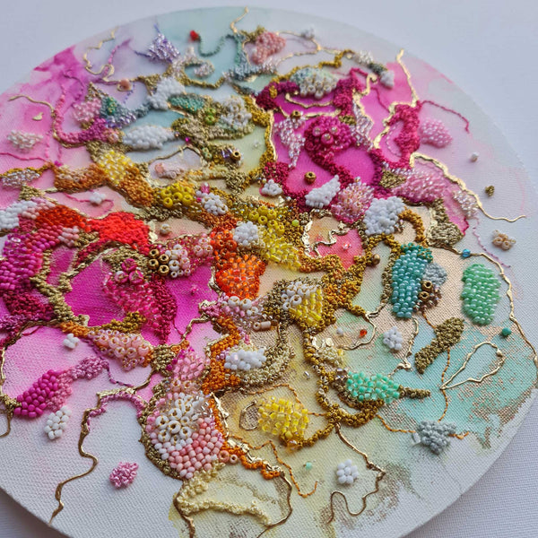 Close-up of a circular mixed media artwork with textured beads and gold threads on colorful pastel background