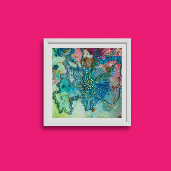 Close-up of colorful hand-stitched embroidery art print in a white frame against pink background