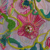 Close-up of hand-stitched embroidery with vibrant pink, green, and blue threads and bead accents on textured fabric.