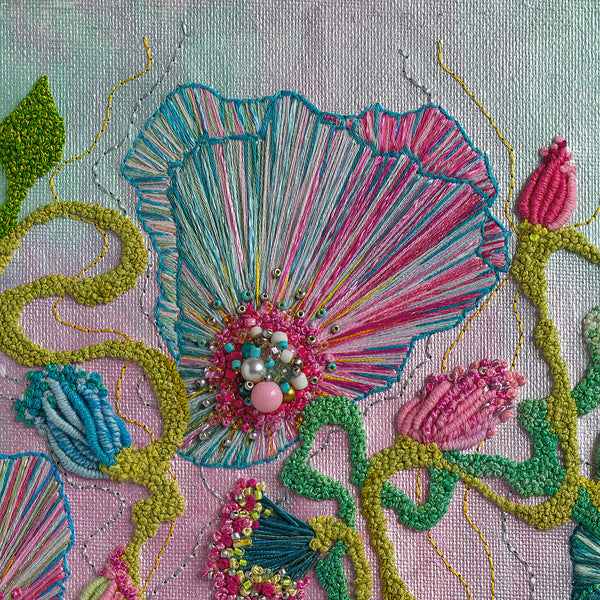 Close-up of hand-stitched embroidery with colorful threads, beads, and textured floral patterns on fabric background