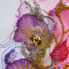 Close-up of hand-stitched Viola Odorata embroidery detail in purple, yellow, and gold threads on textured fabric