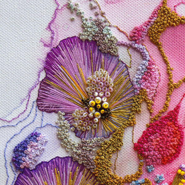 Close-up of hand-stitched Viola Odorata embroidery detail in purple, yellow, and gold threads on textured fabric