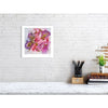 Framed Viola Odorata 2020 fine art print in vibrant pinks and purples displayed on white brick wall above desk.
