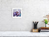 Framed Viola Seven 2023 fine art print with purple embroidery detail displayed on white brick wall above desk.