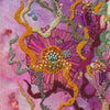 Close-up of hand-stitched embroidery with vibrant pink, orange, and green threads and intricate bead details on fabric.
