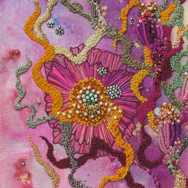 Close-up of hand-stitched embroidery with vibrant pink, orange, and green threads and intricate bead details on fabric.