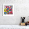 Viola Three 2022 colorful abstract floral fine art print displayed on white brick wall above desk with pencils.