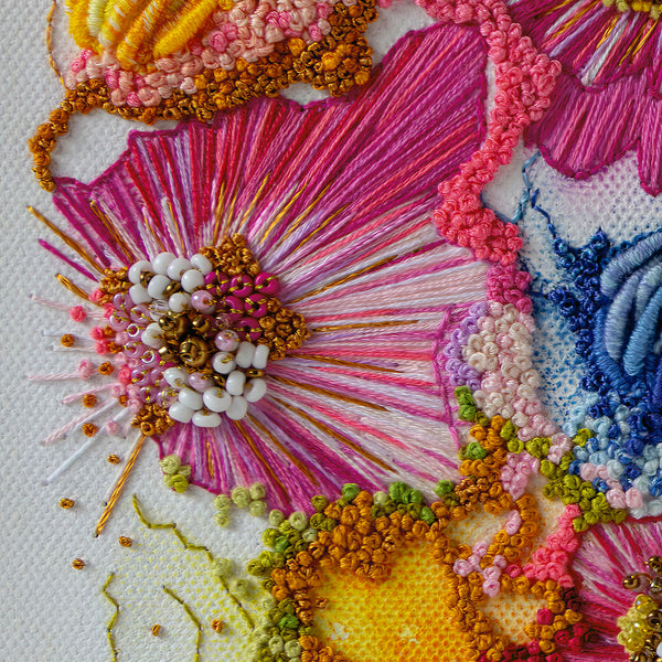Close-up of vibrant hand-stitched embroidery with intricate threads, beads, and textured floral details on fabric.