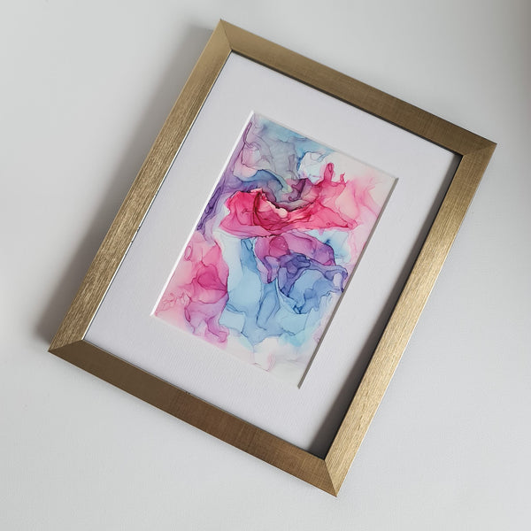 Abstract alcohol ink artwork with flowing pink, purple, and blue hues on Yupo paper in white mount.