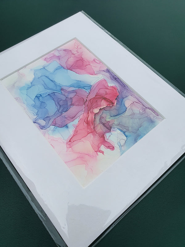Abstract alcohol ink artwork titled Aphrodite Plays with flowing blue, pink, and purple hues on Yupo paper, mounted and sealed.