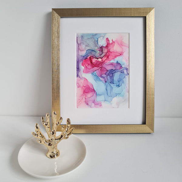 Abstract alcohol ink painting titled Aphrodite Plays 2018 in a gold frame with decorative gold coral on white surface