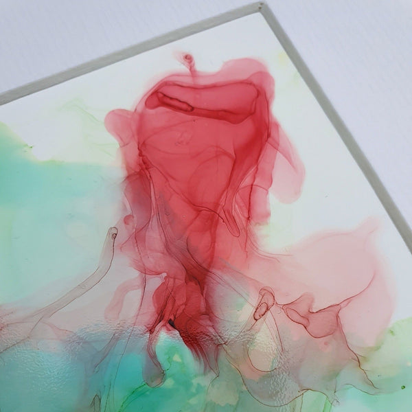 Abstract alcohol ink artwork featuring flowing red and green shapes on Yupo paper in a white mount.