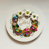 Round coral reef-inspired wreath with beads, faux flowers, embroidery spelling Joy on white canvas background