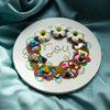 Round coral wreath artwork with beads, faux flowers, embroidery, and gold thread spelling "Joy" in center on white canvas.