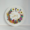Abstract coral reef inspired wreath with white flowers, colorful beads, embroidery, and gold thread spelling "Joy" on canvas