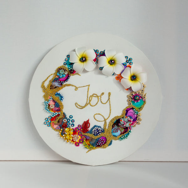 Abstract coral reef inspired wreath with white flowers, colorful beads, embroidery, and gold thread spelling "Joy" on canvas