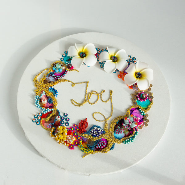 Round coral reef inspired wreath artwork with colorful beads, faux flowers, gold embroidery spelling "Joy" on white canvas