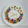 Coral wreath artwork with colorful beads, embroidery, faux flowers, and "Joy" embroidered in gold thread on round canvas.