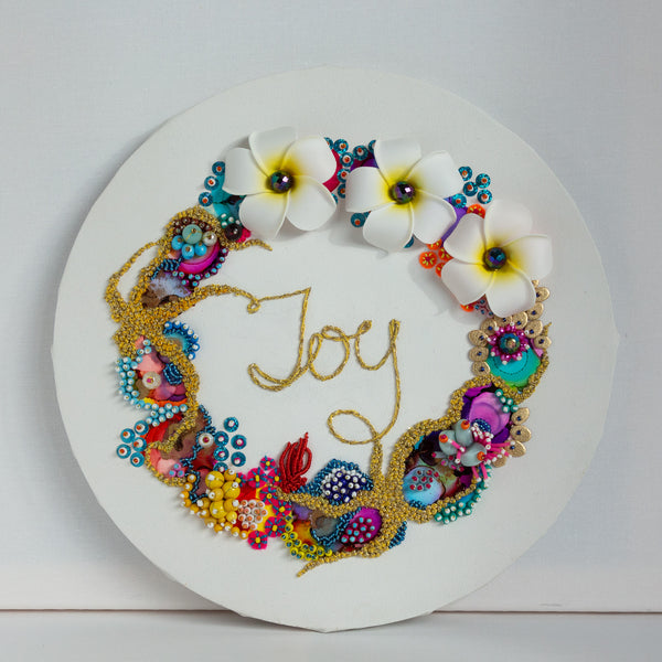 Coral wreath artwork with colorful beads, embroidery, faux flowers, and "Joy" embroidered in gold thread on round canvas.