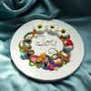 Abstract coral reef-inspired wreath with colorful beads, faux flowers, embroidery, and gold thread spelling "Joy" on round canvas.