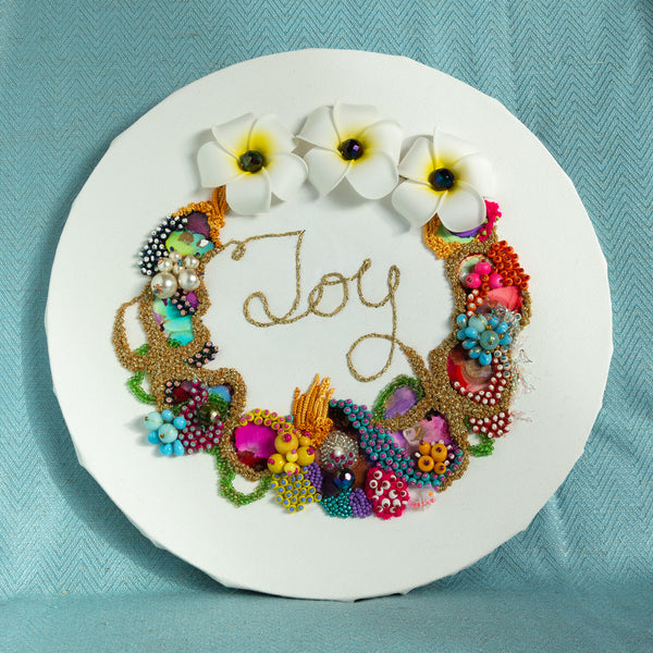 Abstract coral reef-inspired wreath with colorful beads, flowers, and gold embroidery spelling "Joy" on white round canvas