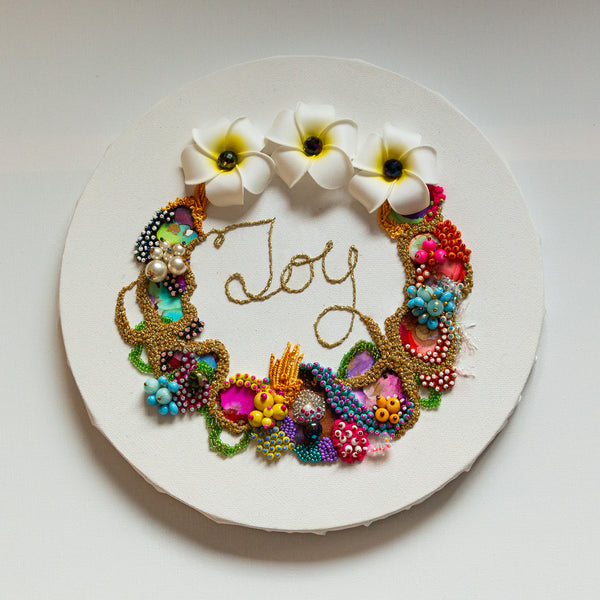 Abstract coral reef-inspired wreath with colorful beads, faux flowers, embroidery, and "Joy" stitched in gold thread.