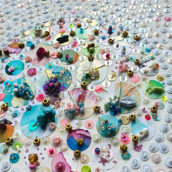 Close-up of upcycled beads and hand-painted sequins arranged on canvas in colorful abstract pattern.