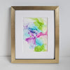 Abstract alcohol ink painting in green, blue, pink, and purple tones mounted in a gold frame on white background.