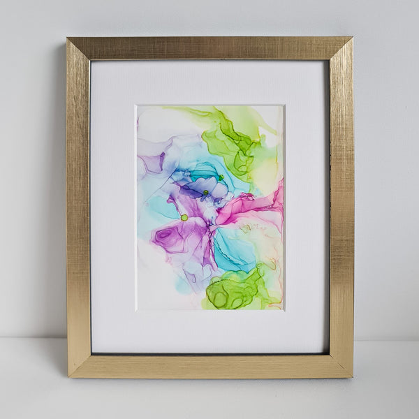 Abstract alcohol ink painting in green, blue, pink, and purple tones mounted in a gold frame on white background.