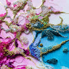 Close-up of hand-embroidered alcohol ink artwork with seed beads and gold thread on canvas, vibrant pink and blue tones.