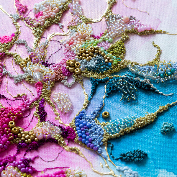 Close-up of hand-embroidered alcohol ink artwork with seed beads and gold thread on canvas, vibrant pink and blue tones.