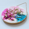 Round mixed media artwork with alcohol ink, hand embroidery, seed beads, and gold leafed edges hanging by a gold chain