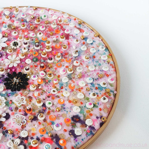 Close-up of Flora 1.0 embroidery art with colorful sequins, beads, pearls, lace flowers on felt in a gold wooden hoop.
