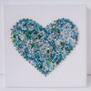 Close-up of a textured mint green and blue beaded heart embroidery on white canvas, handmade art piece.