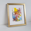 Abstract alcohol ink painting titled Odin's Glory with vibrant colors, mounted in white with a gold frame on a white surface.