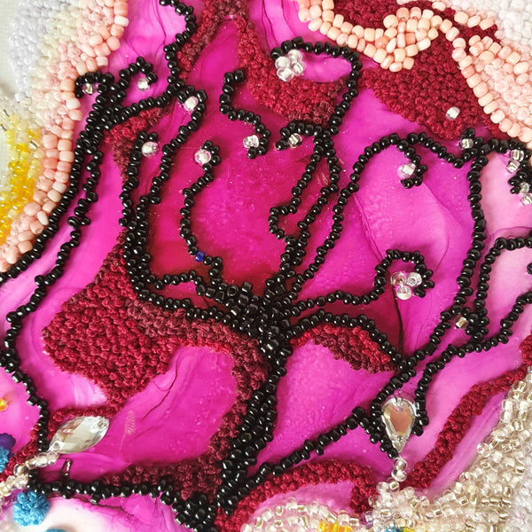 Close-up of intricate beaded embroidery and ink collage artwork in bright pink and red tones on canvas.