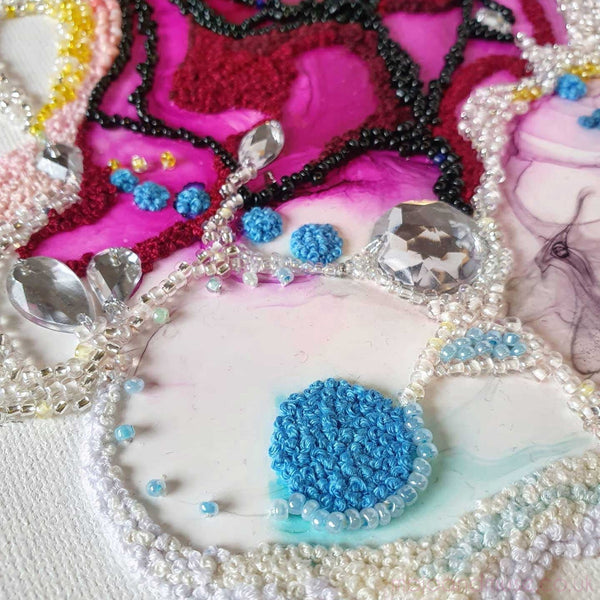 Close-up of intricate collage artwork with embroidery floss, seed beads, gems on canvas in vibrant colors.