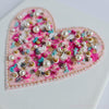 Close-up of Pearl Heart embroidery with beads, pearls, and metallic thread on pink canvas art piece.