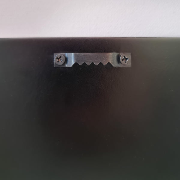 Sawtooth metal hanger attached to the back of a wooden framed artwork for wall mounting.