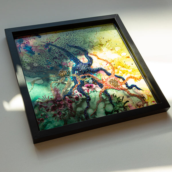 Framed resin artwork featuring colorful beaded and embroidered starfish inspired by tide pools, with layered alcohol ink details.