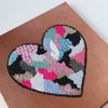 Heart-shaped embroidery with beads and acrylic spray paint on canvas, bright multicolor design on brown background.